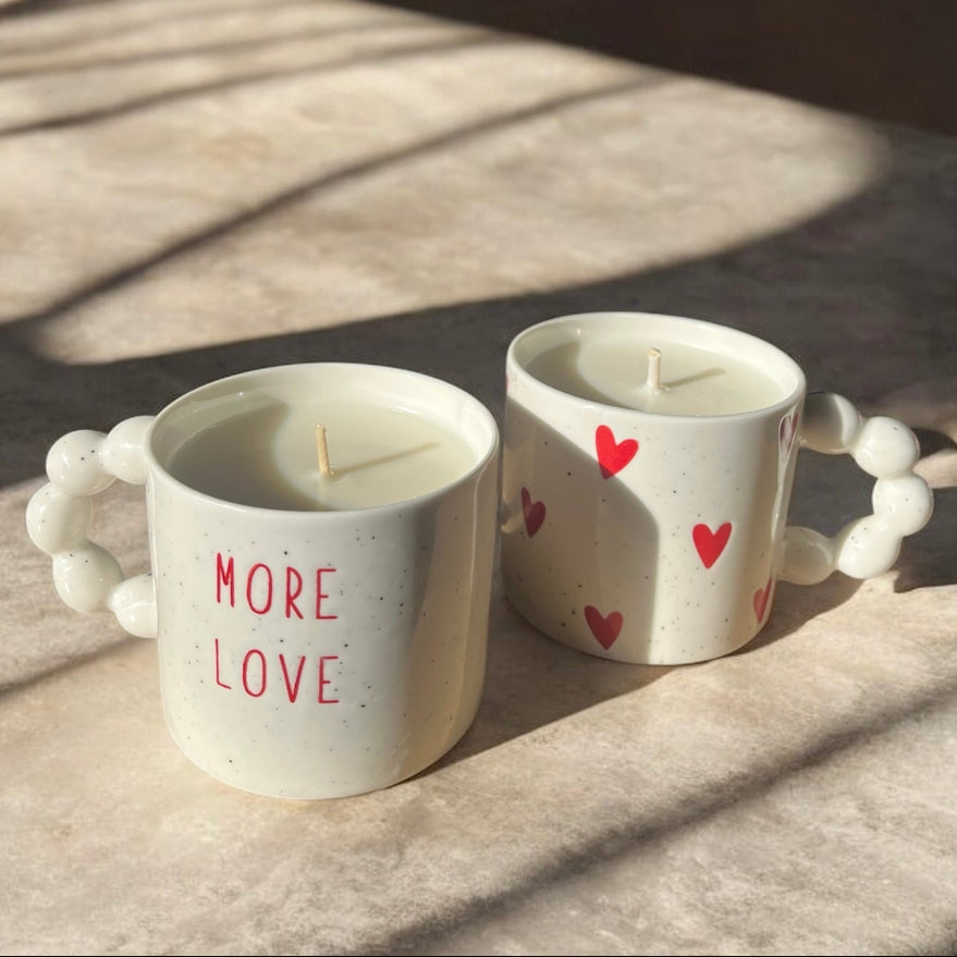 2 bougies coulées dans des tasses en céramique, l'une avec des coeurs, l'autre avec une inscription "more love". Parfum fleur de coton, contenance 340ml. 